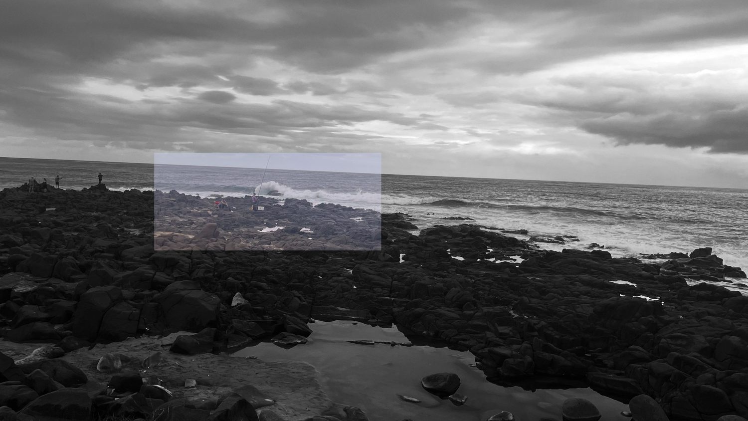 Monochrome rocky coastline with a rectangle of restored colour revealing anglers on the rocks